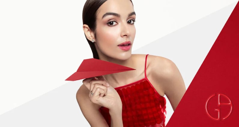 A woman grips a red paper airplane, looking excited as she prepares to send it flying